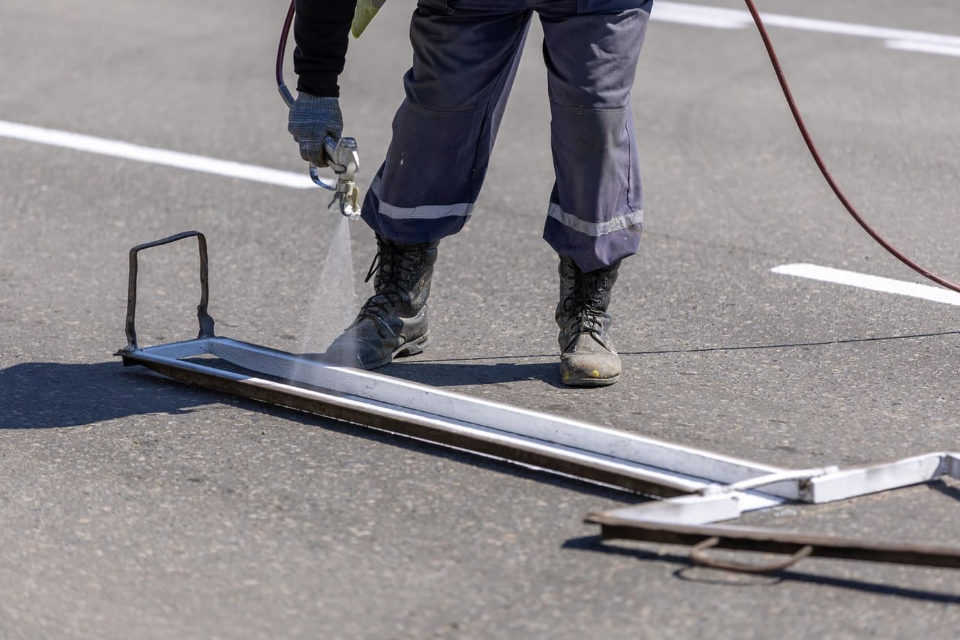 Line marker spraying a crisp white car park bay line through a steel template